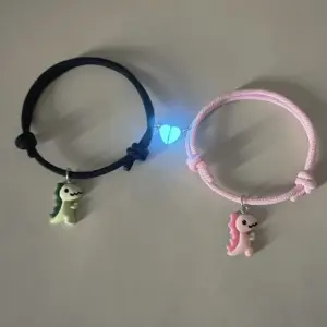 Zwei Armbänder mit Dinosaurier-Anhängern in Schwarz und Rosa mit Herz-Element