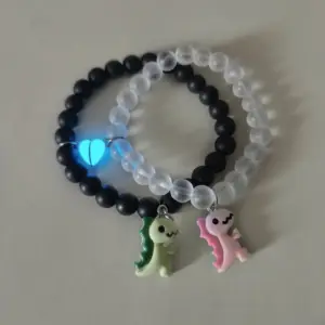 Zwei Armbänder aus schwarzen und milchig weißen Perlen mit Dinosaurier-Anhängern und Herzen