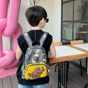 Junge mit Sonnenbrille trägt grauen Rucksack mit Dinosaurier-Muster und gelbem Frontfach