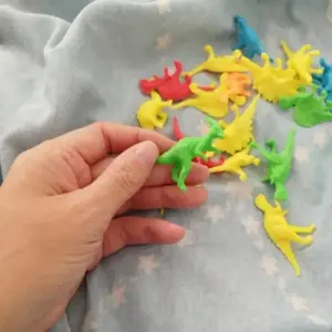 Hand hält bunte kleine Dinosaurier-Figuren